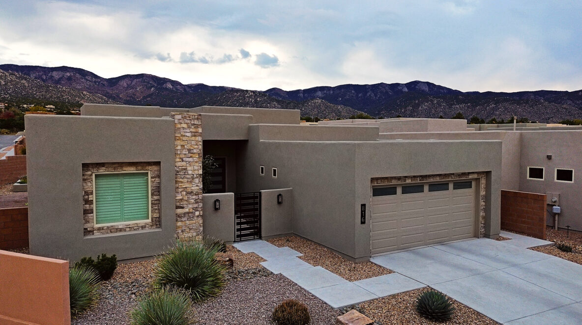 An aerial photo of a traditional New Mexico flat-roofed home with a synthetic stucco finish, with the majestic Sandia Mountains in the background.