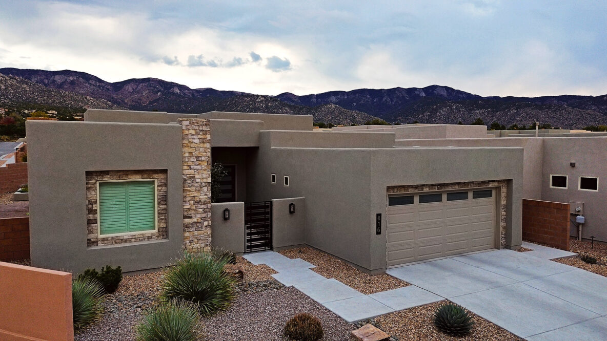 An aerial photo of a traditional New Mexico flat-roofed home with a synthetic stucco finish, with the majestic Sandia Mountains in the background.