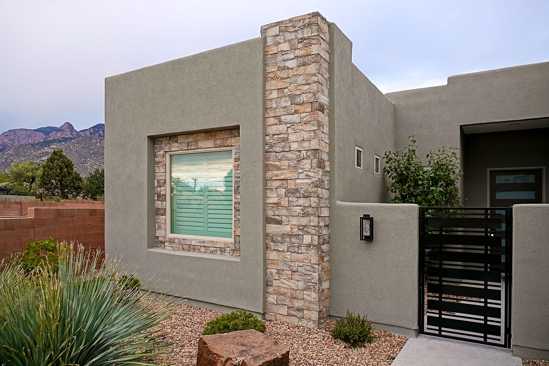 Modern flat-roofed home in North-eastern Albuquerque featuring grey stucco finish and stacked stone accents.